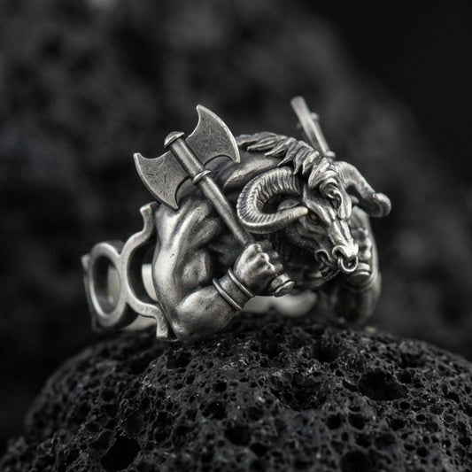 Detailed Minotaur ring crafted in oxidized sterling silver, muscular bull-headed beast holding double axe, macro product shot on textured volcanic rock background