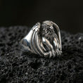 Load image into Gallery viewer, Polished silver griffin signet ring featuring guardian beast with folded wings and detailed claws, centered close-up on dark porous volcanic stone
