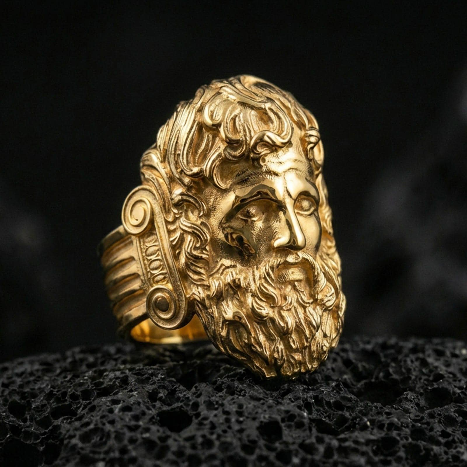 Gold plated Zeus signet ring with high-relief Greek god head and intricate hair detailing, premium studio macro on black volcanic rock surface