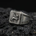 Load image into Gallery viewer, Detailed gryphon signet ring crafted in oxidized sterling silver, winged guardian creature emblem with sunburst background, macro product shot on textured volcanic rock
