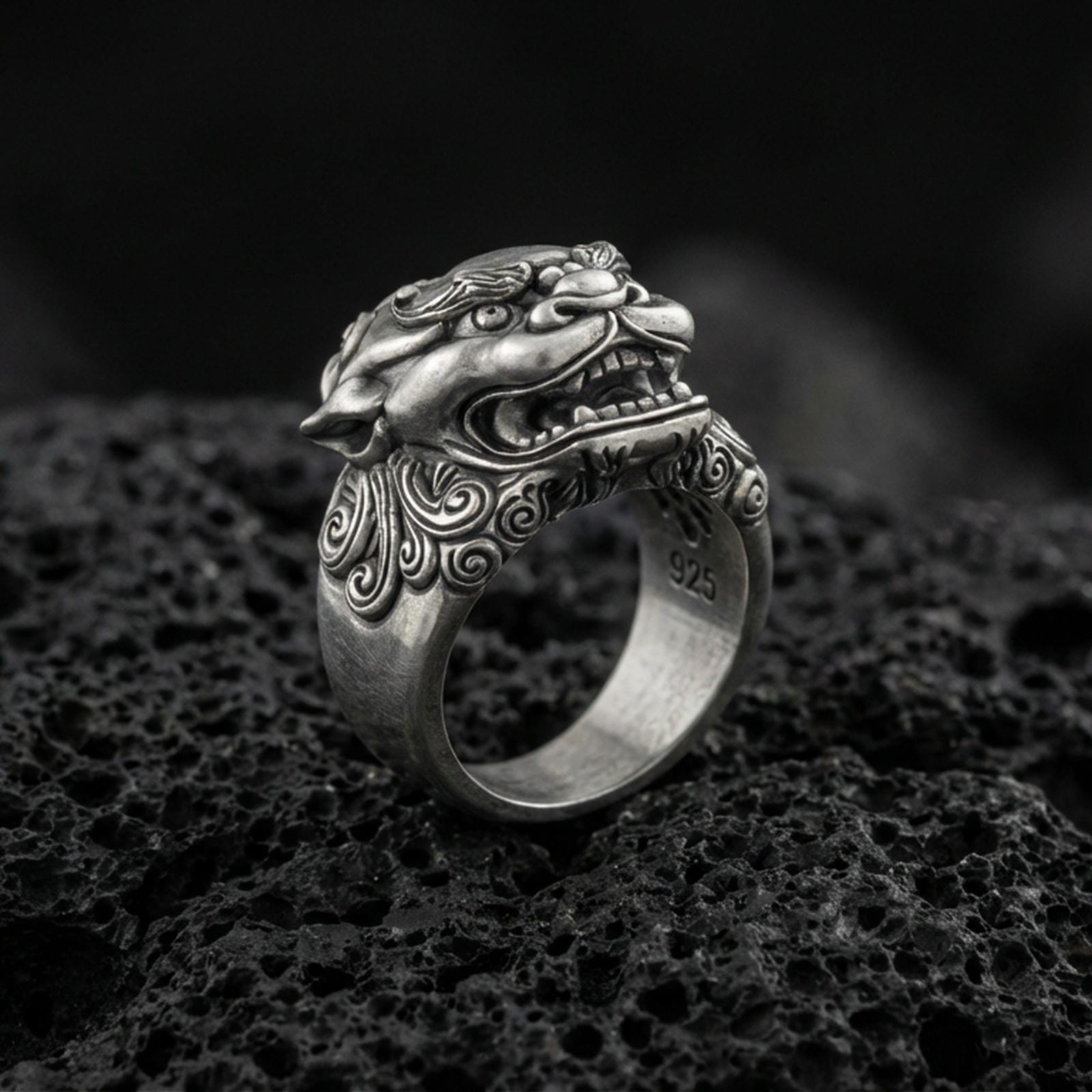 Detailed Foo Dog ring crafted in oxidized sterling silver, fierce Chinese guardian lion head with ornate swirl engravings, macro product shot on textured volcanic rock background