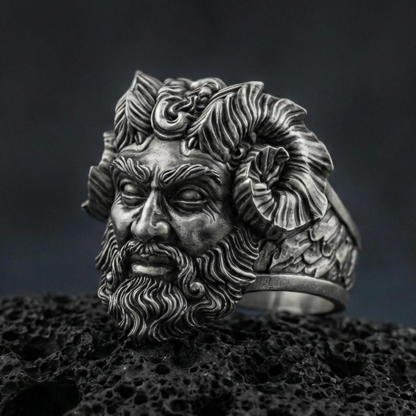 Detailed Czernobog ring crafted in oxidized sterling silver, Slavic dark deity face with horned crown and flowing beard, macro product shot on textured volcanic rock background