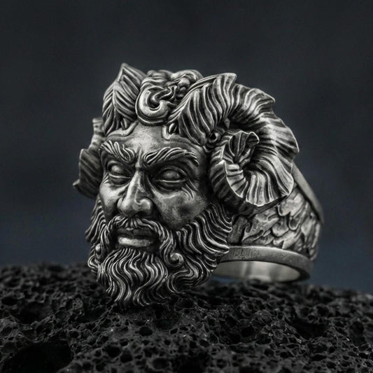 Detailed Czernobog ring crafted in oxidized sterling silver, Slavic dark deity face with horned crown and flowing beard, macro product shot on textured volcanic rock background