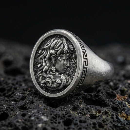 Detailed Medusa signet ring crafted in oxidized 925 sterling silver, snake hair portrait with Greek key border, macro product shot on textured volcanic rock background