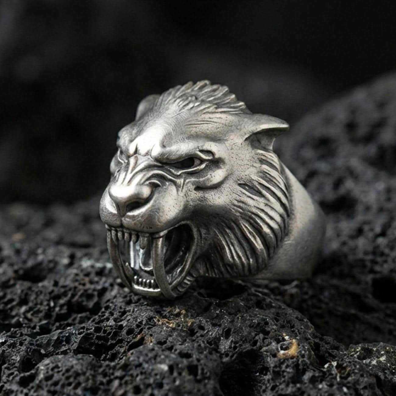 Detailed werewolf head ring crafted in oxidized sterling silver, snarling wolf face with sharp fangs, macro product shot on textured volcanic rock background
