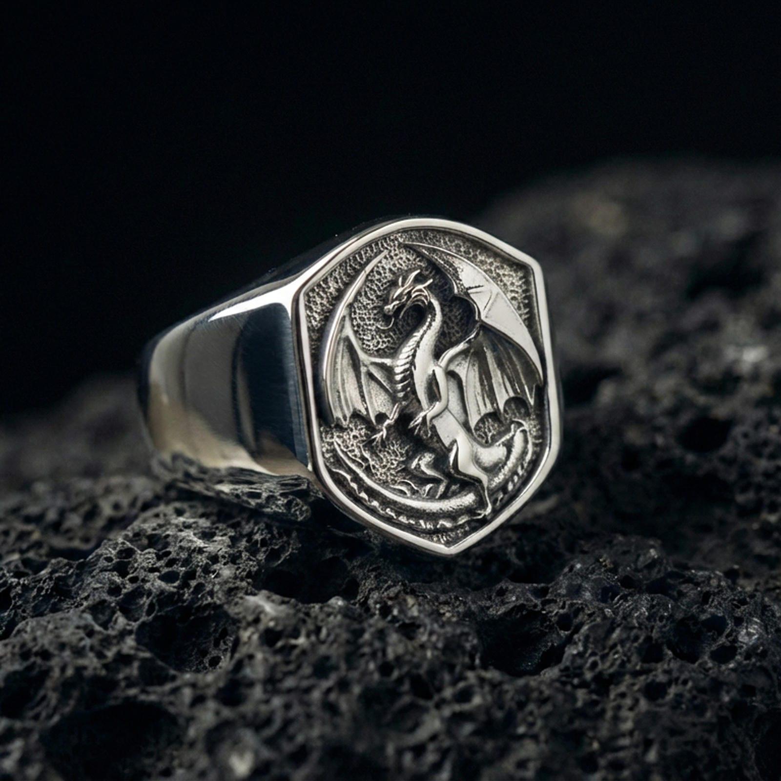 Polished sterling silver dragon signet ring on black volcanic stone, detailed winged dragon engraving, bold fantasy accessory
