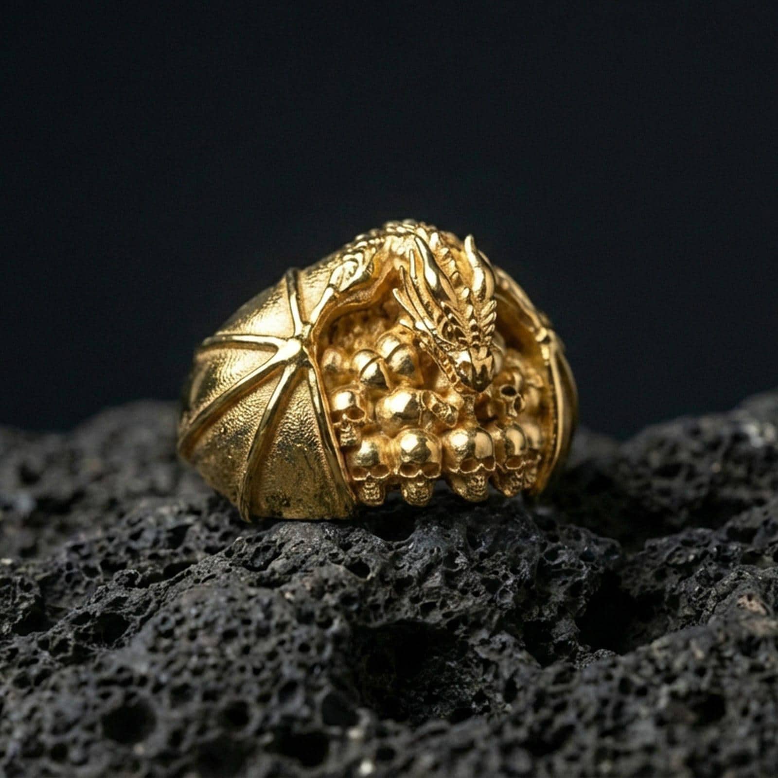Gold plated dragon skull signet ring on black volcanic stone, mythical dragon over skulls, bold gothic design