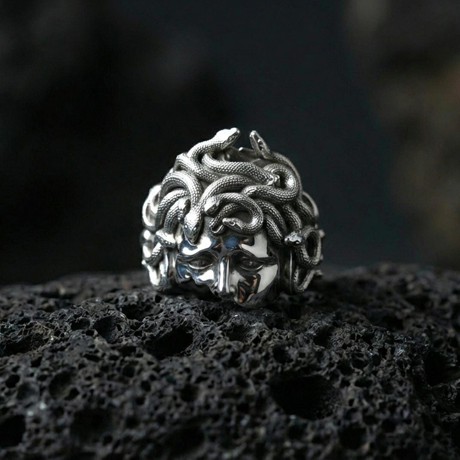 Polished sterling silver Medusa head ring on black volcanic stone, detailed snake crown and goddess face, mythological statement ring