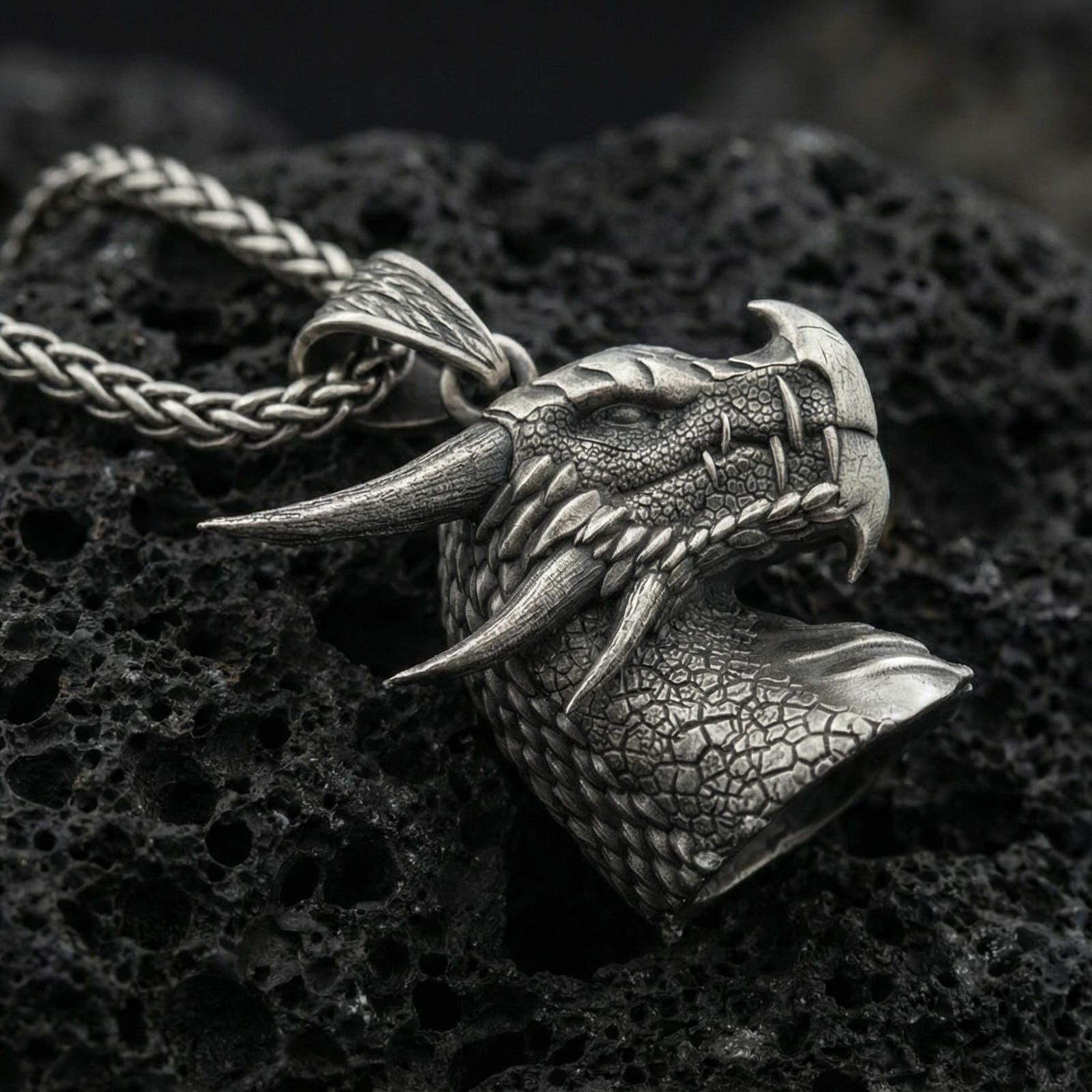 Oxidized sterling silver dragon pendant on textured volcanic rock, detailed scale pattern and horns, macro studio shot