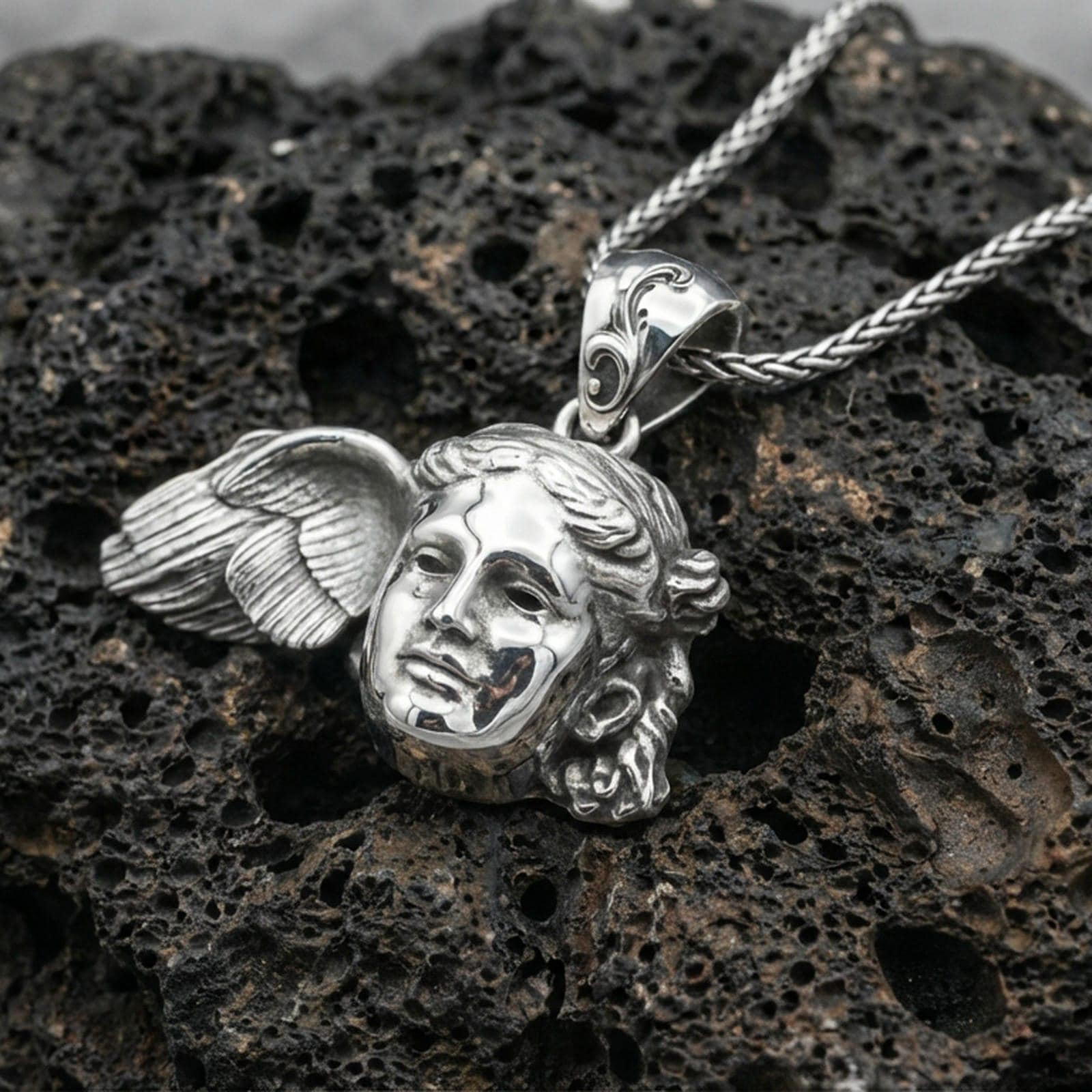 Polished silver Hypnos medallion pendant on dark volcanic stone, crisp facial sculpture and wing relief, premium close-up composition