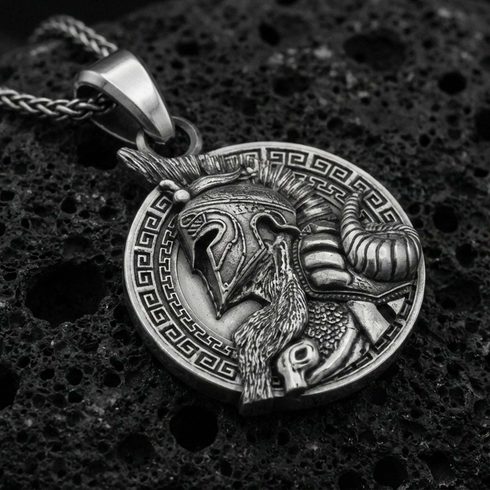 Oxidized sterling silver Viking warrior pendant on textured volcanic rock, Norse helmet profile relief with Greek key border, macro studio shot