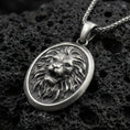 Load image into Gallery viewer, Oxidized sterling silver roaring lion oval pendant on textured volcanic rock, sculpted mane relief and raised lion face, macro studio shot
