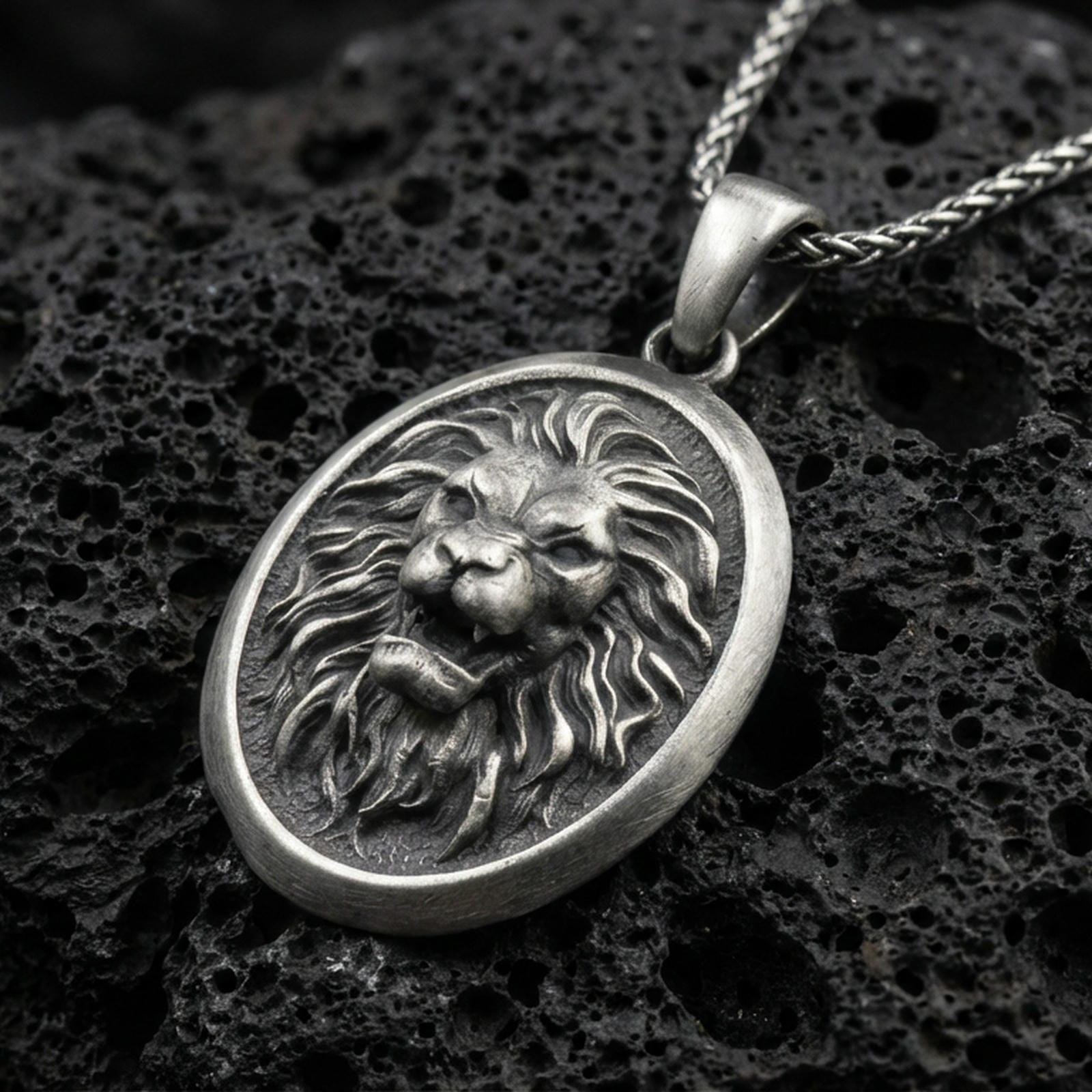 Oxidized sterling silver roaring lion oval pendant on textured volcanic rock, sculpted mane relief and raised lion face, macro studio shot