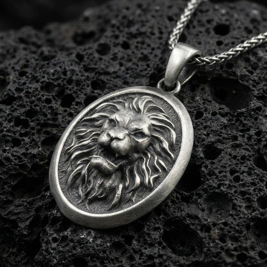 Oxidized sterling silver roaring lion oval pendant on textured volcanic rock, sculpted mane relief and raised lion face, macro studio shot