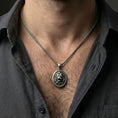 Load image into Gallery viewer, Oxidized sterling silver roaring lion pendant worn on neck on a braided chain, centered chest framing, moody lifestyle studio shot
