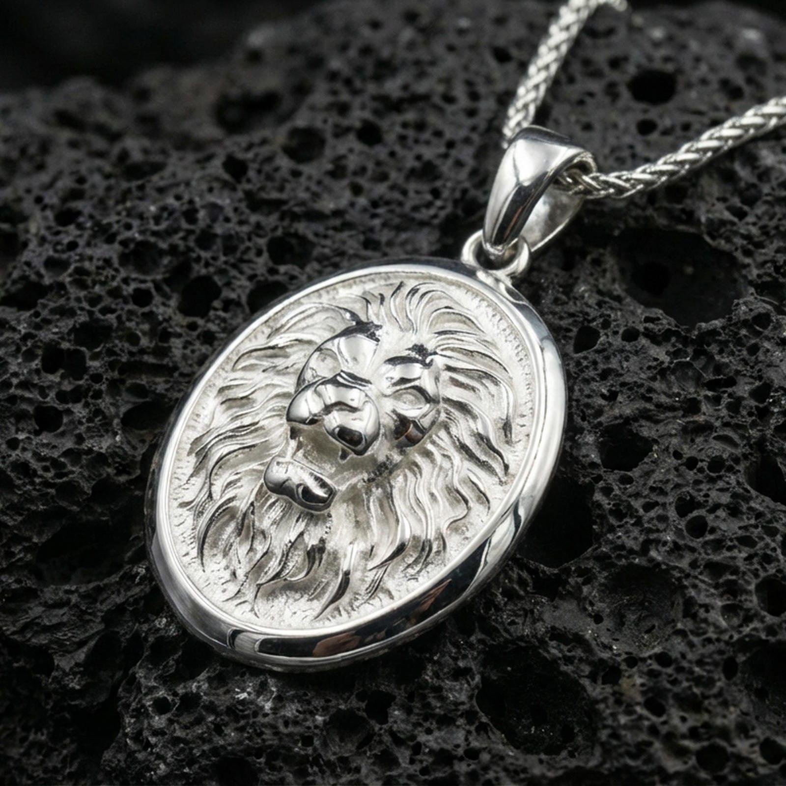 Polished silver lion head oval pendant necklace on dark volcanic stone, crisp mane detail and smooth bezel edge, premium close-up composition