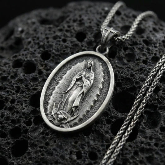 Oxidized sterling silver Our Lady of Guadalupe oval pendant on textured volcanic rock, raised Virgin Mary relief with radiant frame, macro studio shot