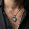 Load image into Gallery viewer, Oxidized sterling silver Our Lady of Guadalupe pendant worn on neck on a braided chain, centered chest framing, moody lifestyle studio shot
