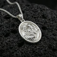 Load image into Gallery viewer, Polished silver Holy Family medallion necklace on dark volcanic stone, crisp engraved faces and smooth oval bezel, premium close-up composition
