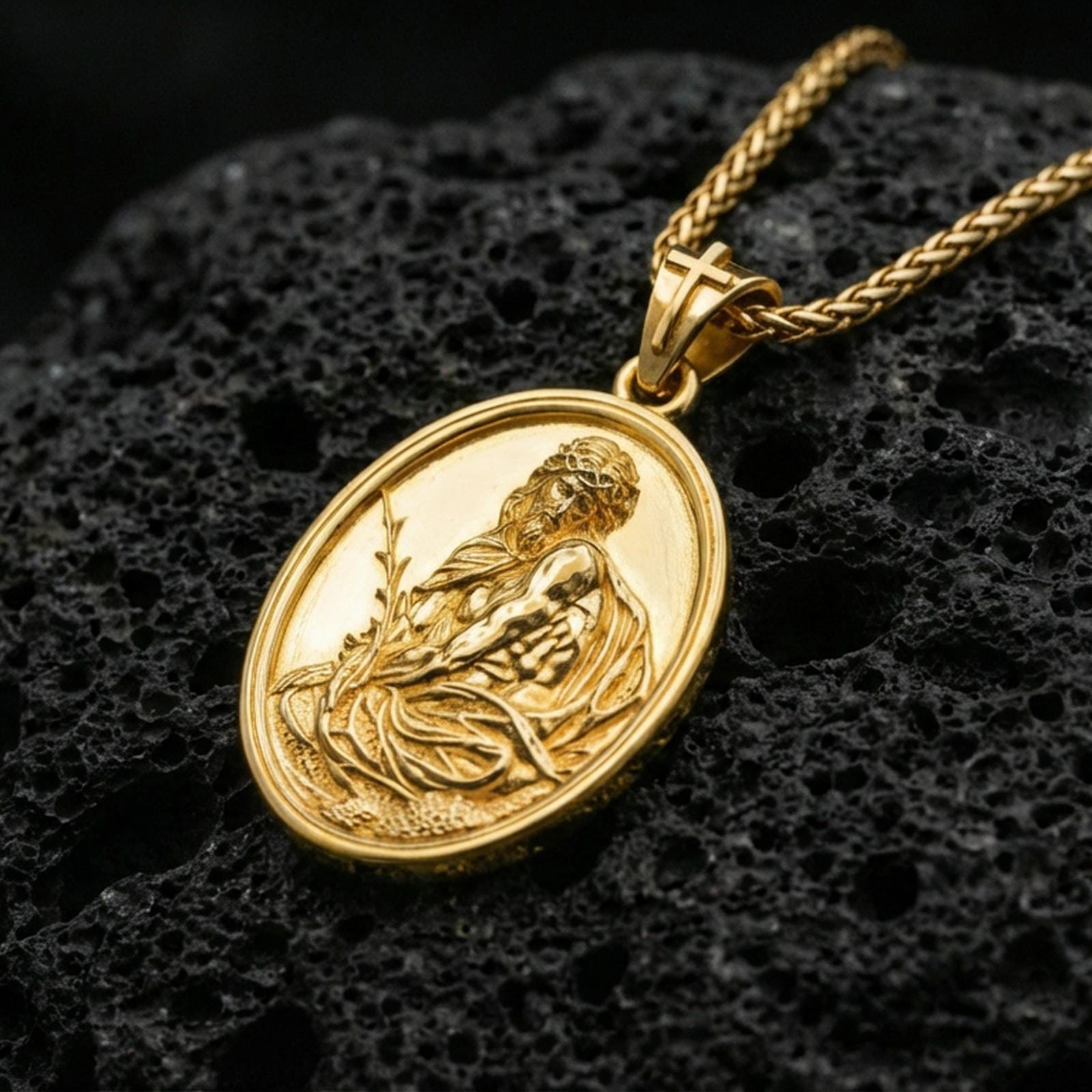 Gold plated Jesus Christ pendant on porous volcanic rock backdrop, devotional oval medal with detailed relief and antique styling, high-contrast lighting