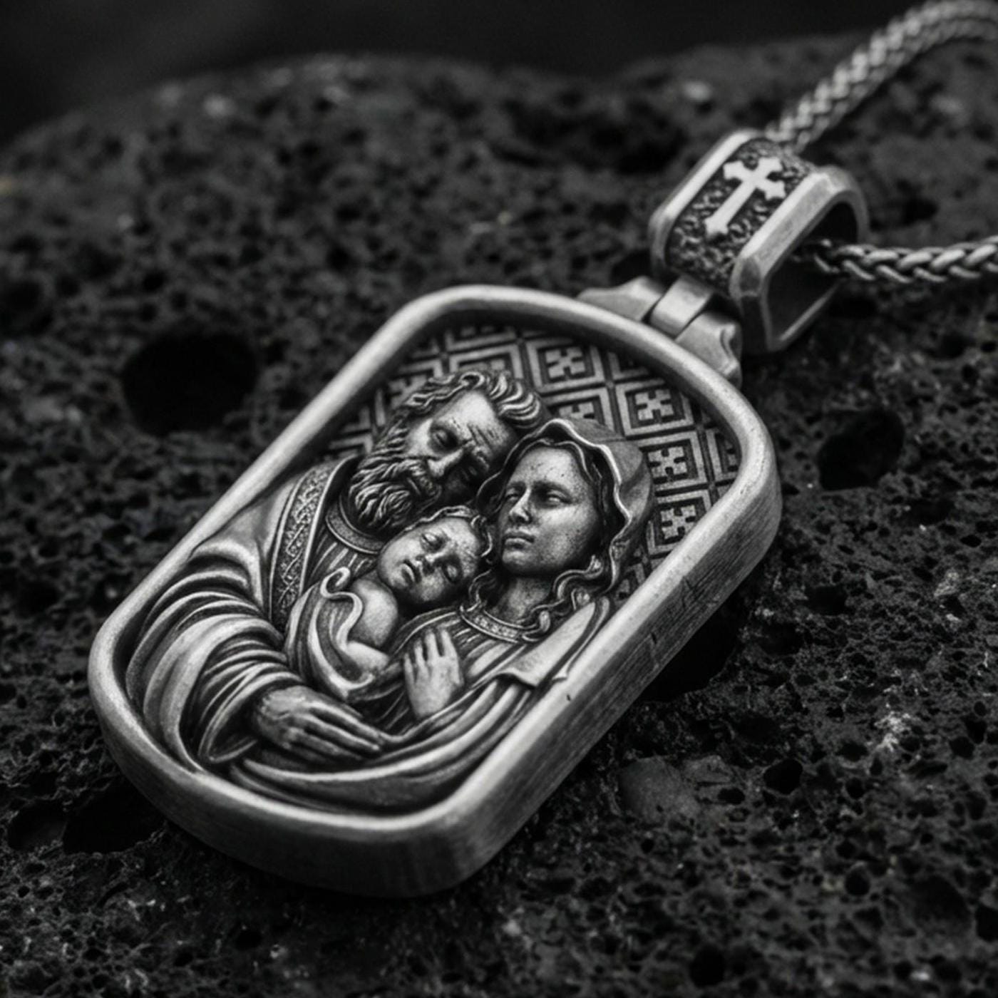 Oxidized sterling silver Holy Family pendant on textured volcanic rock, rectangular medallion with Mary Joseph and Child relief, macro studio shot