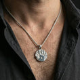 Load image into Gallery viewer, Polished silver Dark Brotherhood handprint necklace worn on neck, close lifestyle crop, clear emblem relief and textured skull pattern
