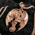 Load image into Gallery viewer, Rose gold plated dragon cross pendant on matte volcanic stone, detailed dragon scales and skull accent on ornate cross, sharp macro focus
