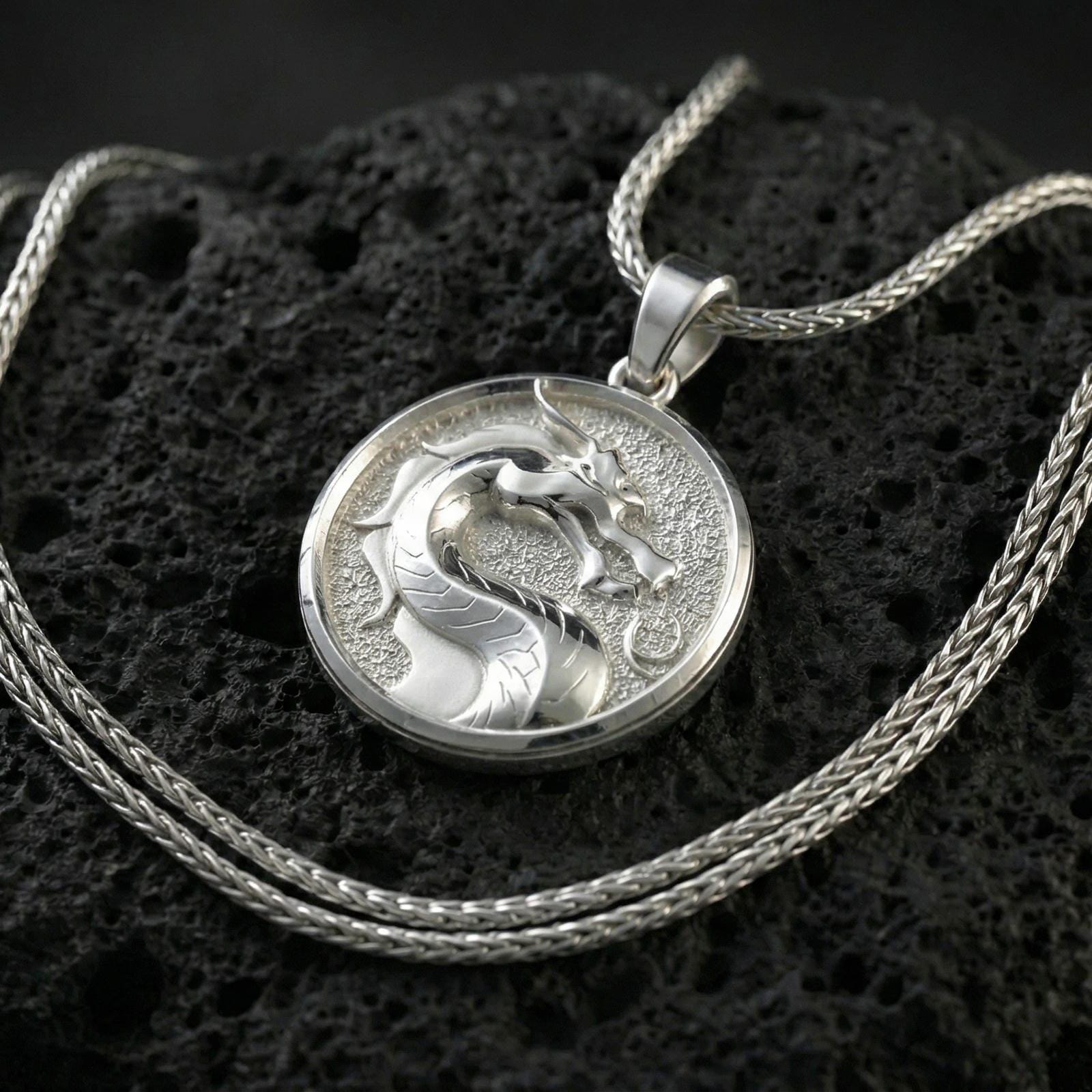 Polished silver Mortal Kombat dragon medallion necklace on textured volcanic stone, crisp circular border and engraved background, close-up shot