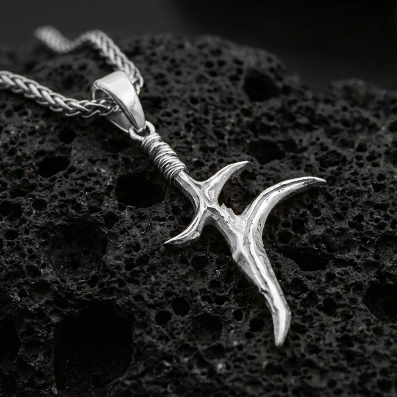 Polished silver black knife dagger pendant on porous volcanic stone, minimal blade charm necklace with wrapped handle, close-up