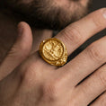 Load image into Gallery viewer, Gold plated roman eagle signet ring worn on a finger, dark background with focus on the laurel and emblem relief
