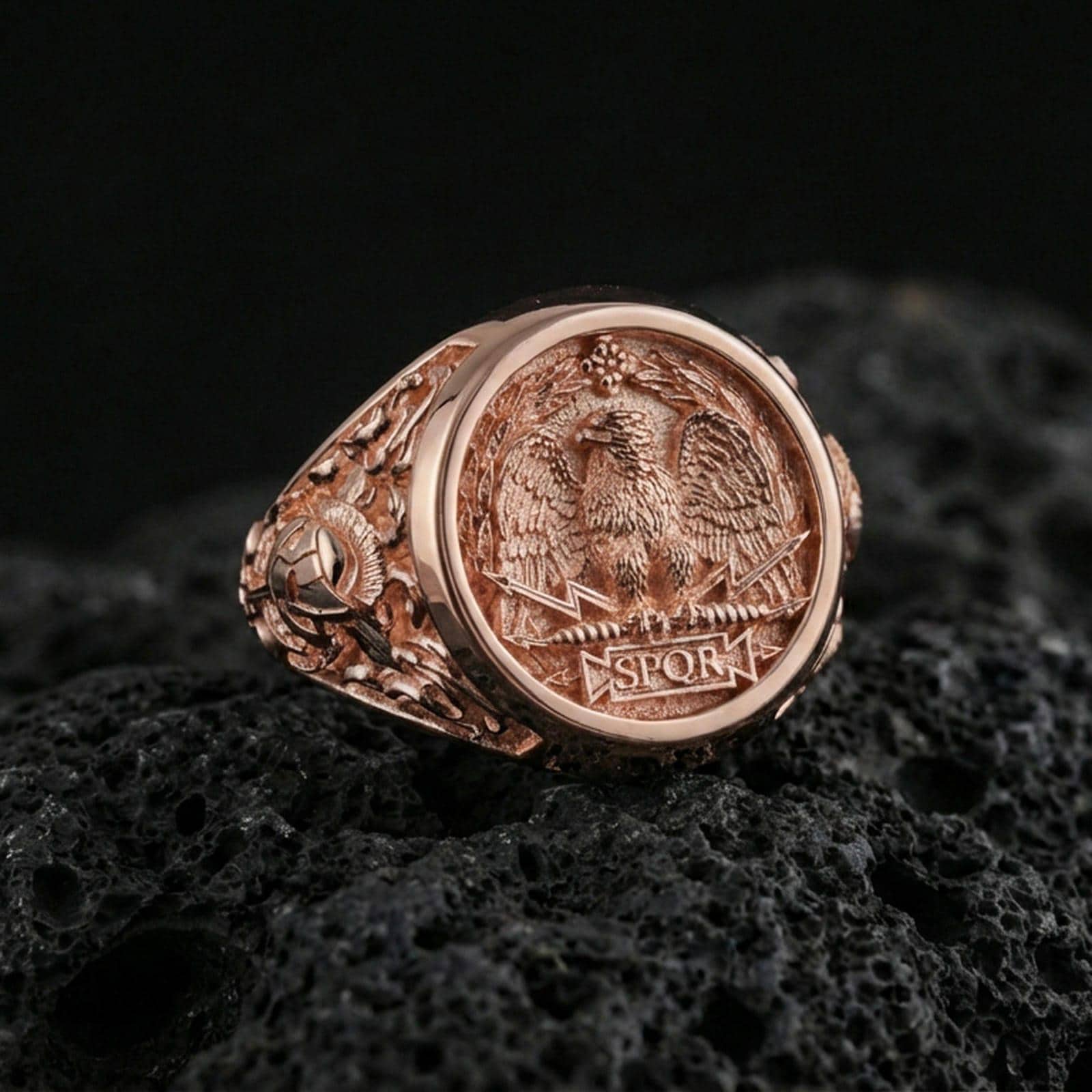 Rose gold plated roman eagle ring on porous volcanic rock, premium studio lighting with shallow depth of field