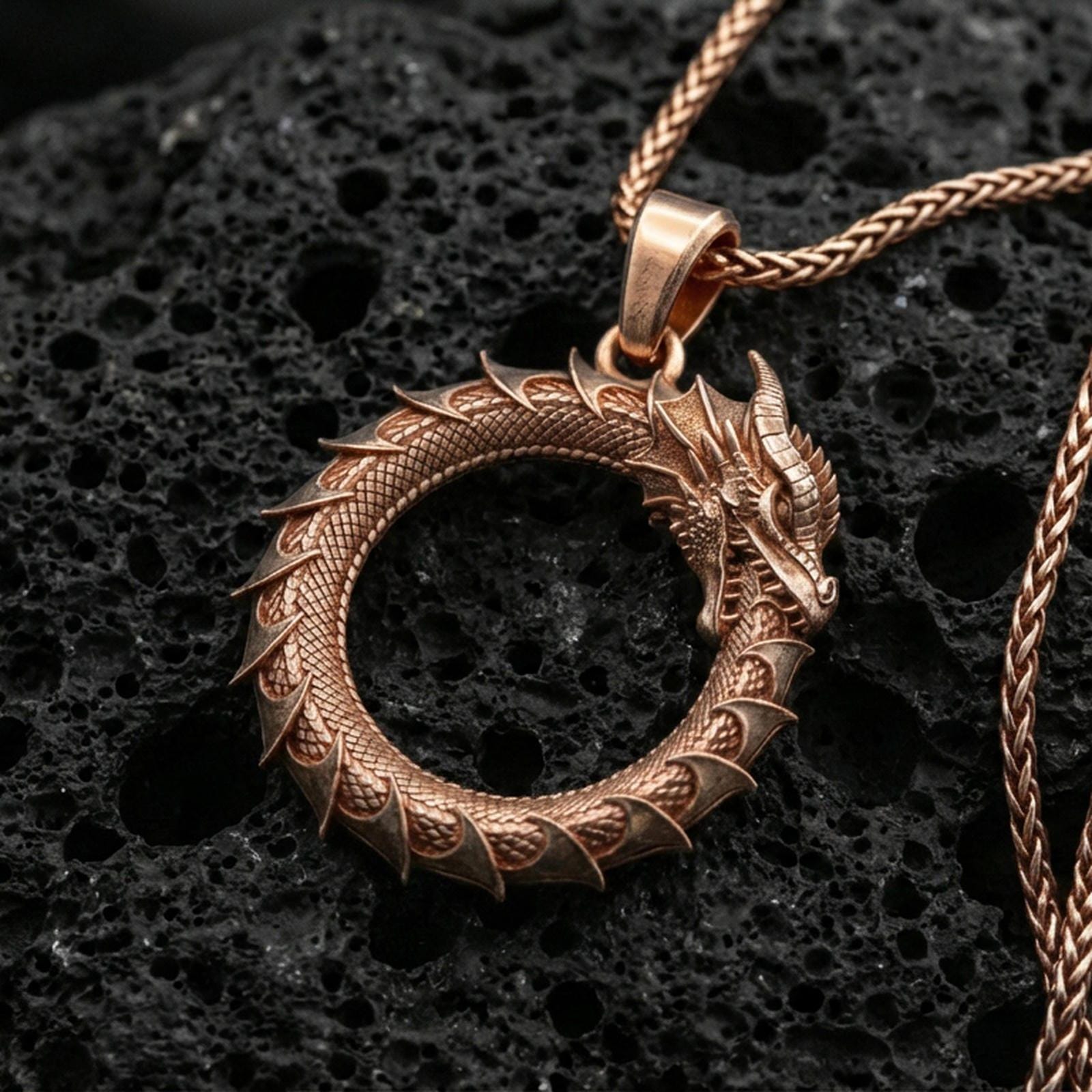 Rose gold plated ouroboros dragon circle pendant on volcanic stone surface, tail-biting dragon eternity necklace, sharp detail