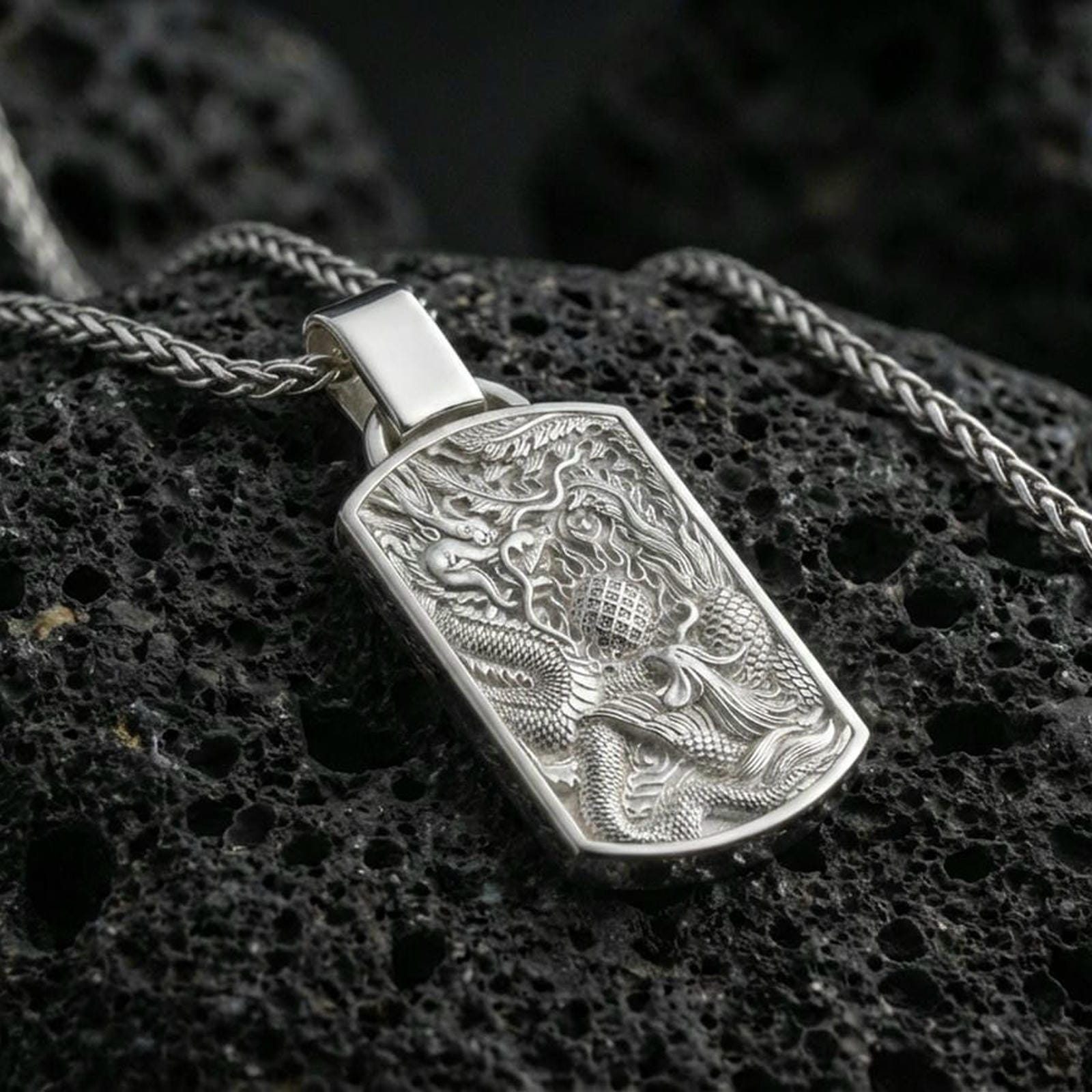 Polished silver dragon phoenix pendant necklace on porous volcanic stone, yin yang symbol relief, premium close-up