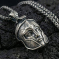 Load image into Gallery viewer, Oxidized sterling silver Greek helmet pendant necklace on black volcanic rock, macro close-up highlighting the warrior faceplate details and dark antique depth
