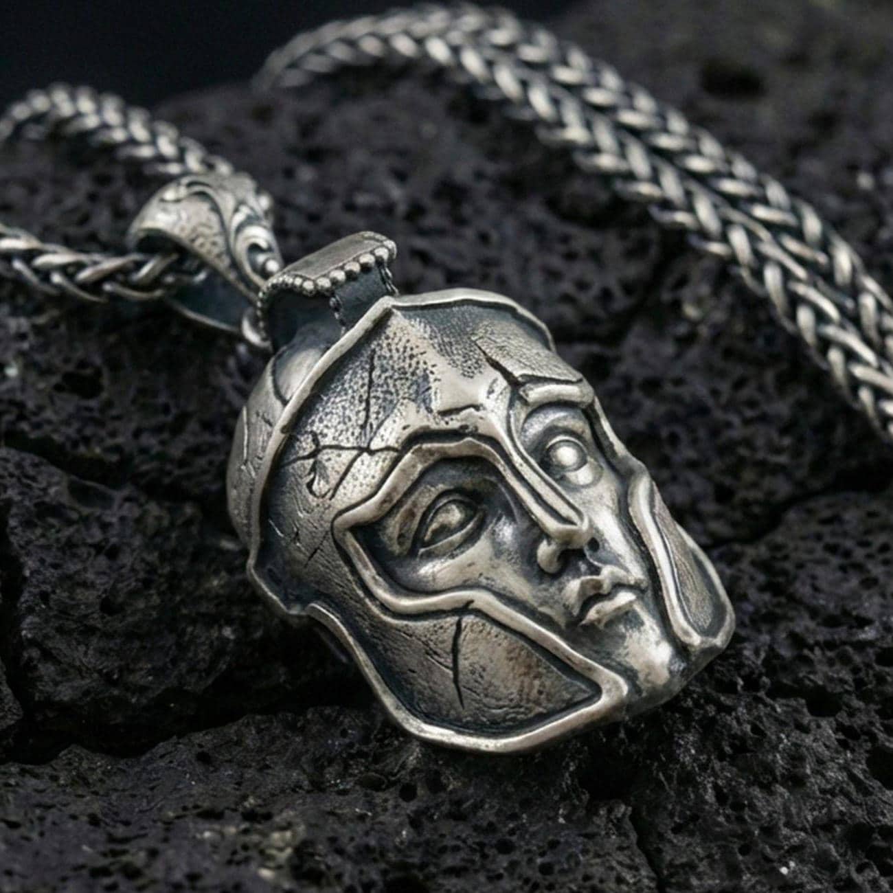 Oxidized sterling silver Greek helmet pendant necklace on black volcanic rock, macro close-up highlighting the warrior faceplate details and dark antique depth