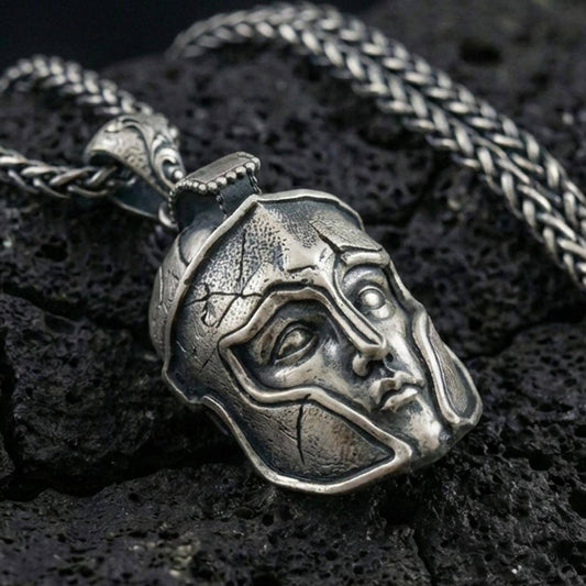 Oxidized sterling silver Greek helmet pendant necklace on black volcanic rock, macro close-up highlighting the warrior faceplate details and dark antique depth