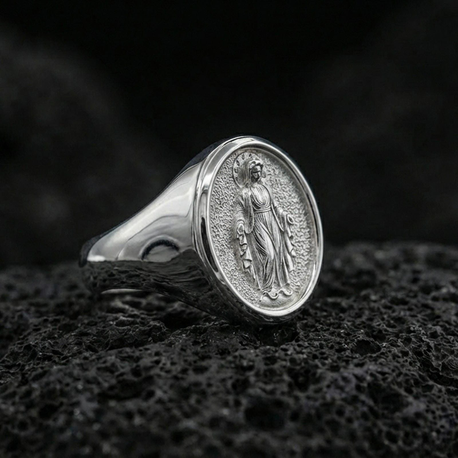 Polished silver Virgin Mary oval signet ring on porous volcanic stone, Catholic devotional ring, studio close-up