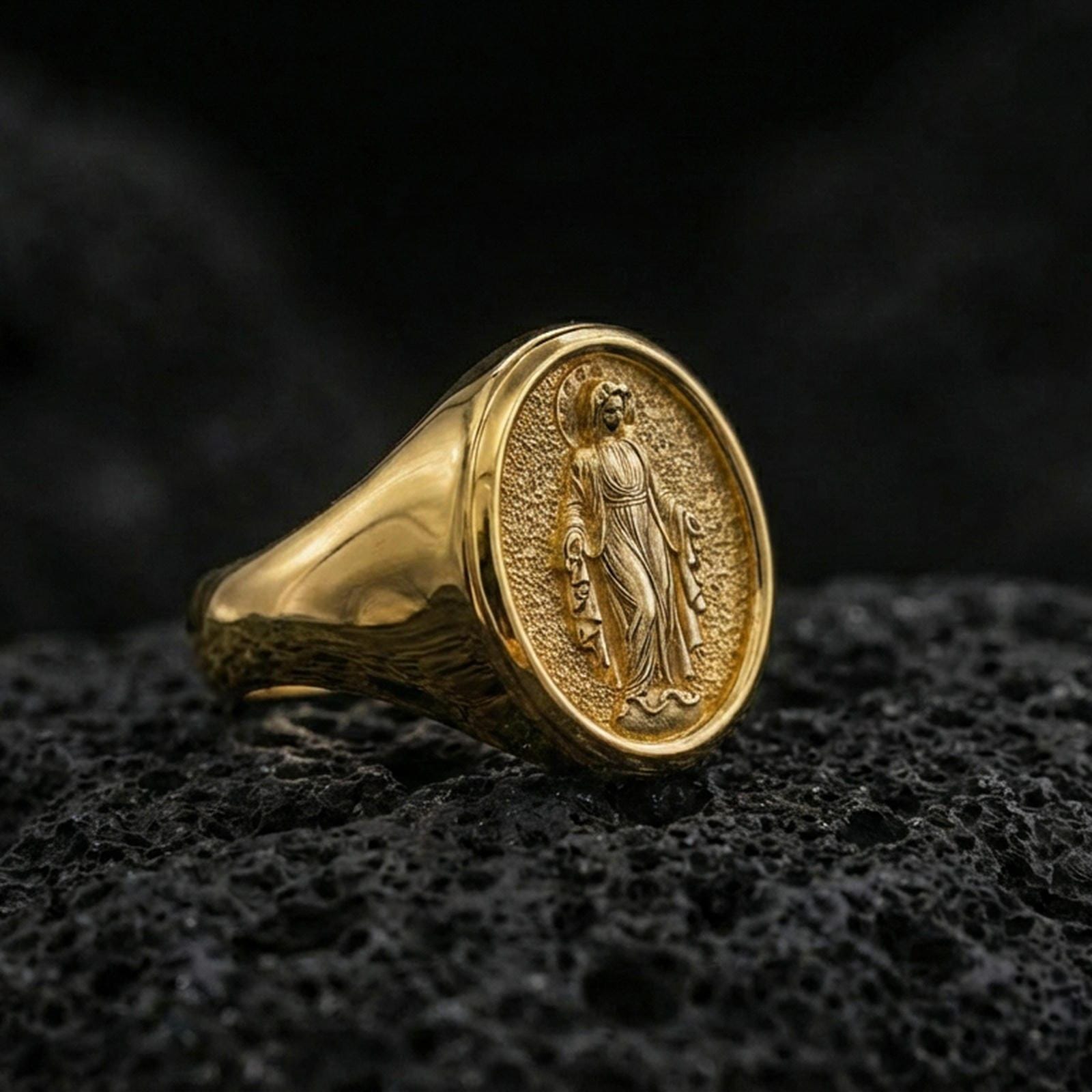 Gold plated Virgin Mary signet ring on dark volcanic rock, oval medallion religious ring, sharp macro detail