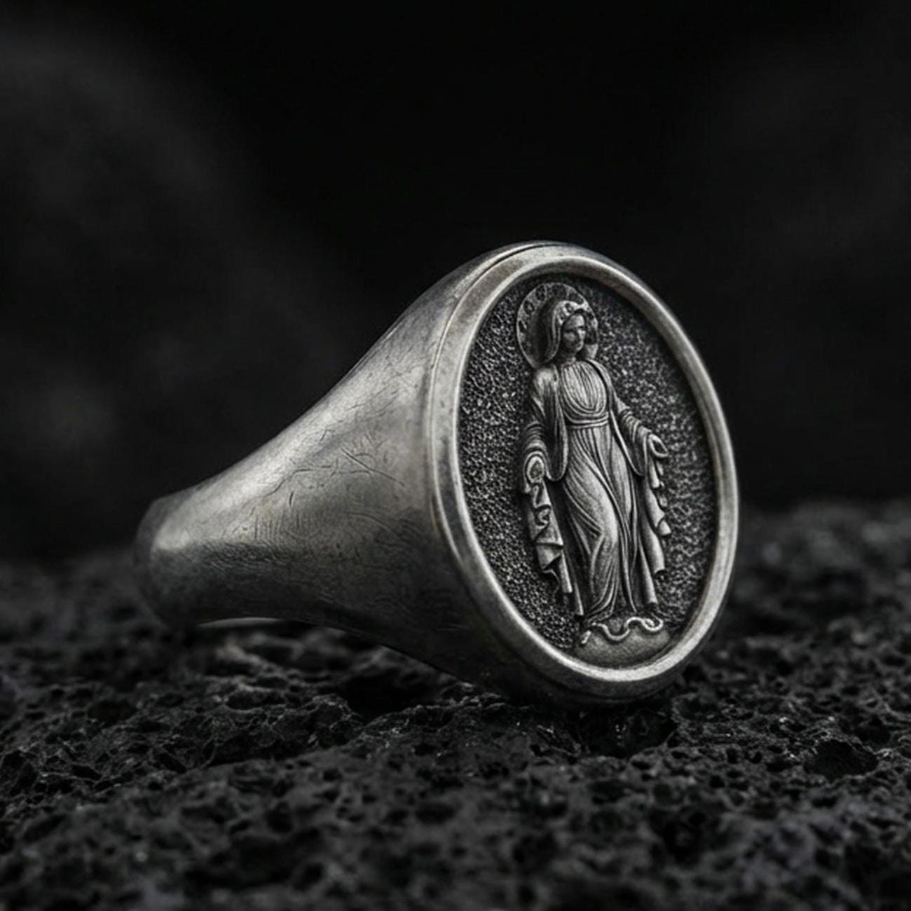 Oxidized sterling silver Virgin Mary signet ring on volcanic rock, oval religious medal face, macro product photo
