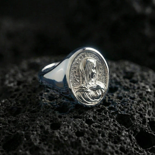 Polished silver Virgin Mary oval signet ring on porous volcanic stone, reflective religious ring, studio close-up