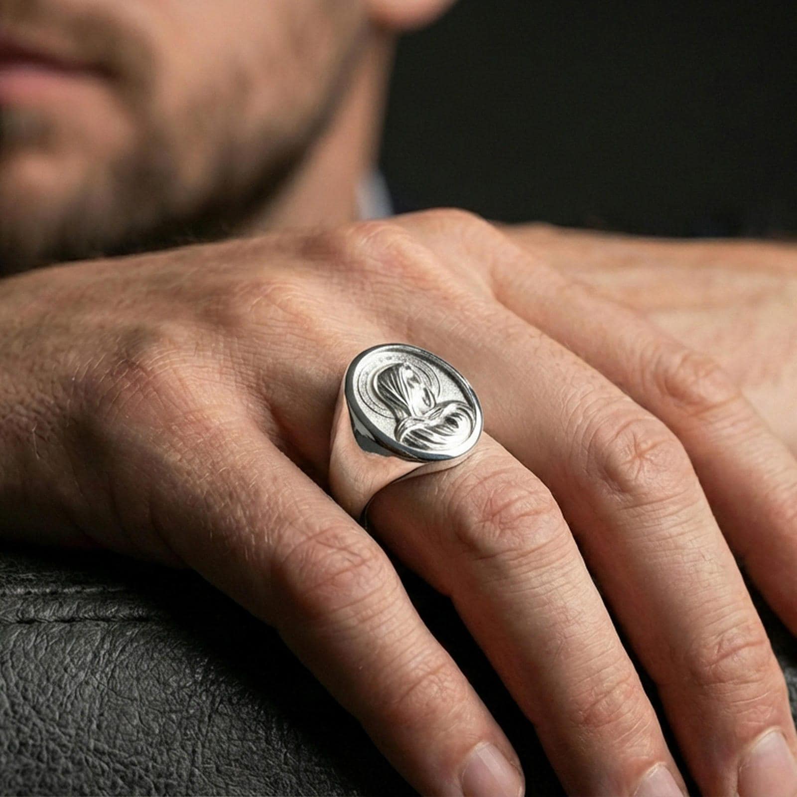 Polished silver Virgin Mary oval signet ring worn on finger, shiny Marian medal face, minimalist lifestyle crop