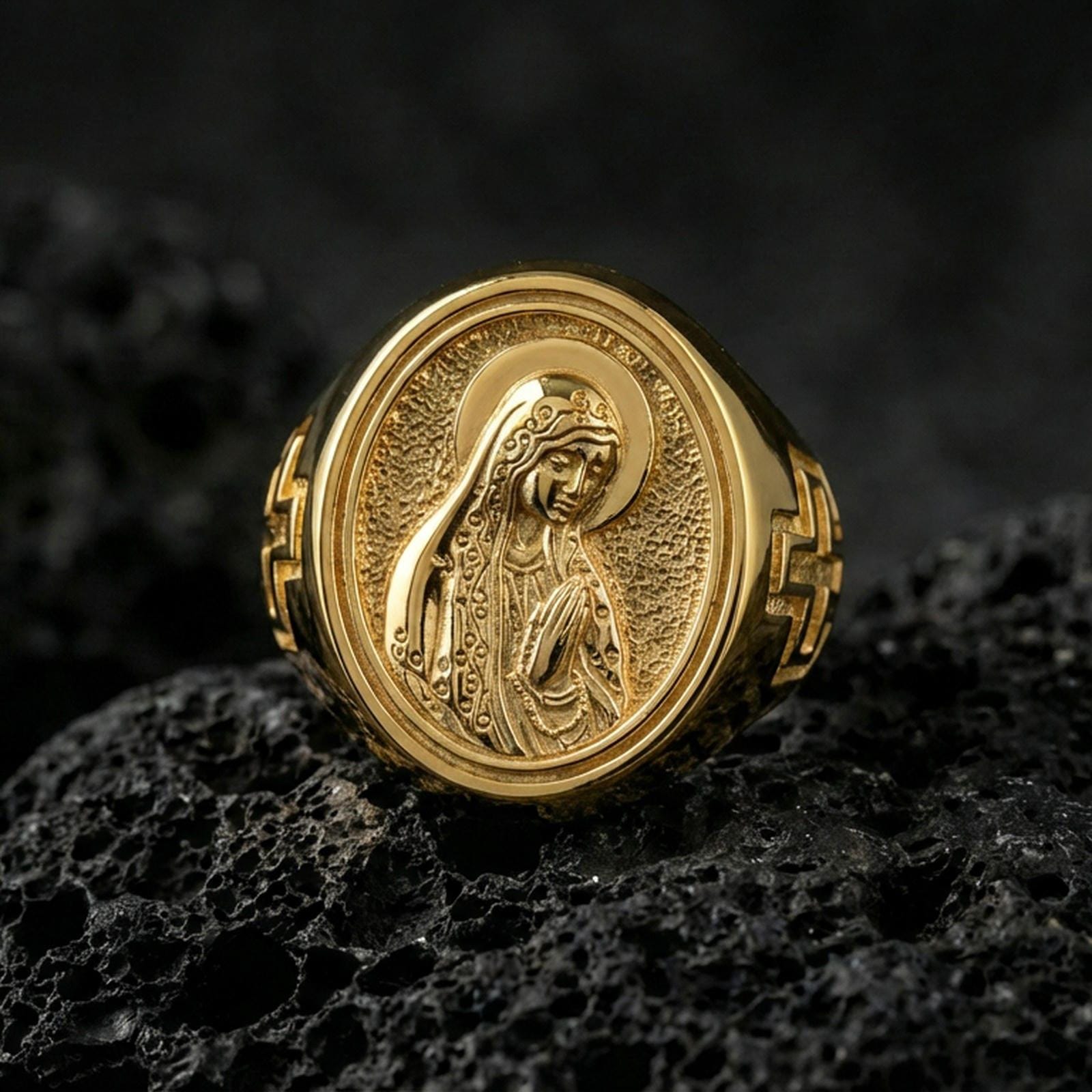Gold plated Our Lady of Guadalupe signet ring on dark volcanic rock, oval Marian cameo face, premium macro photo