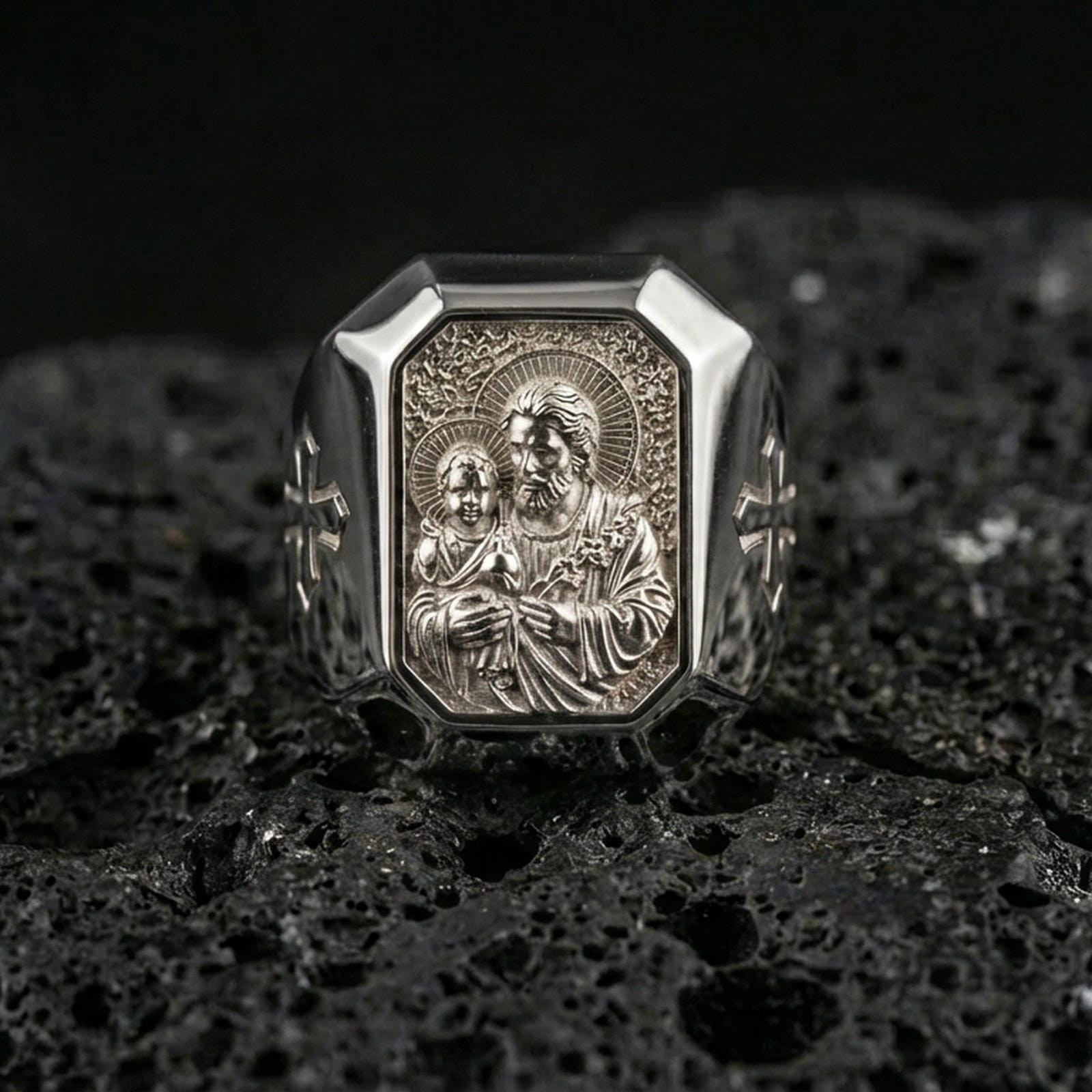 Polished silver St Joseph signet ring on porous volcanic stone, octagonal bezel, detailed saint medal engraving close-up
