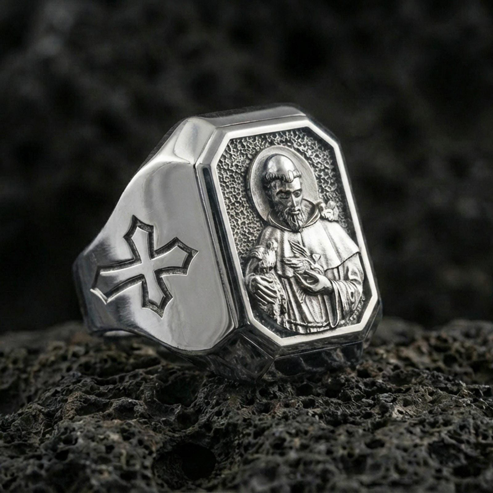 Polished silver St Francis ring on porous volcanic stone, detailed saint halo relief, Christian signet style