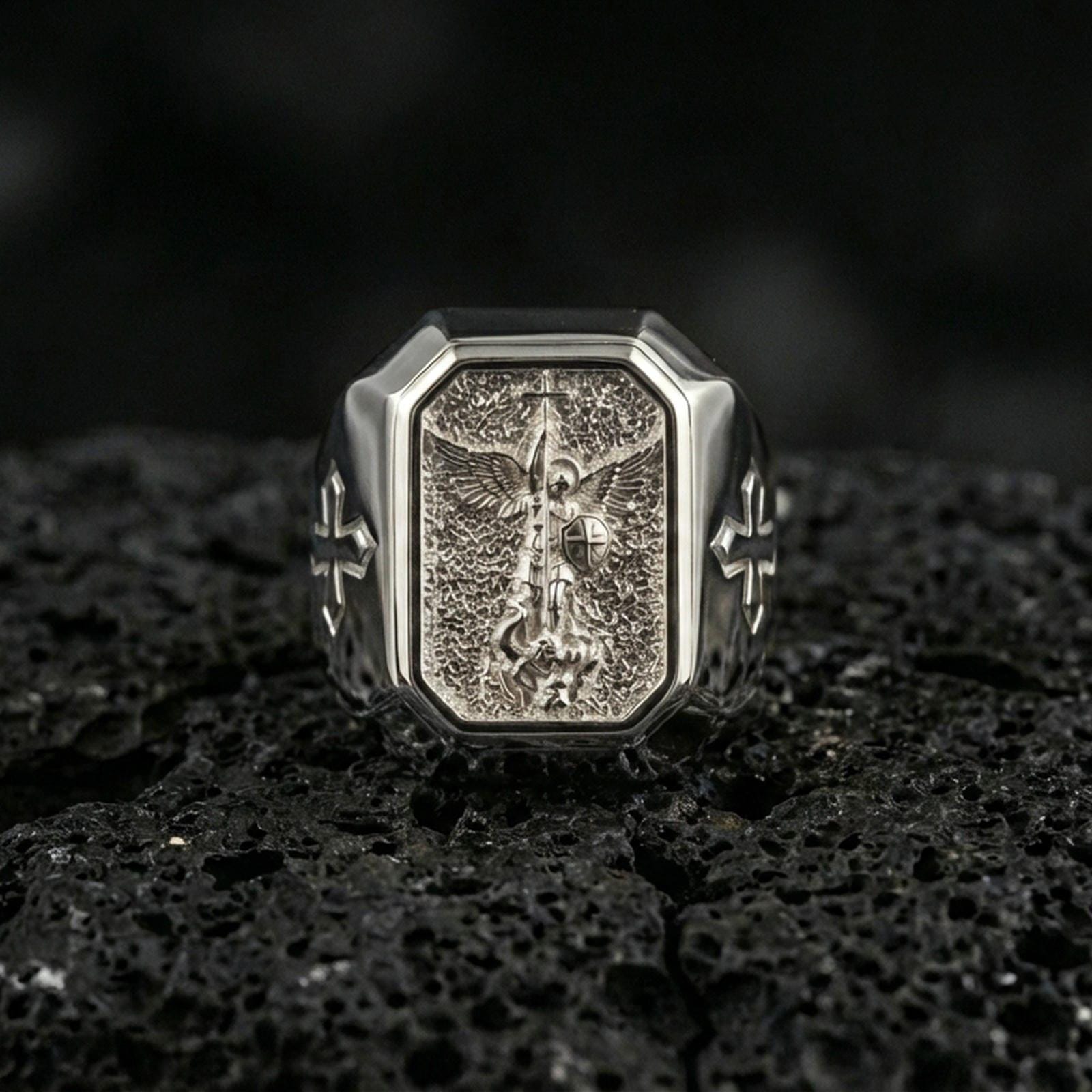 Polished silver St Michael archangel signet ring on porous volcanic stone, angel spear and shield relief, Christian ring