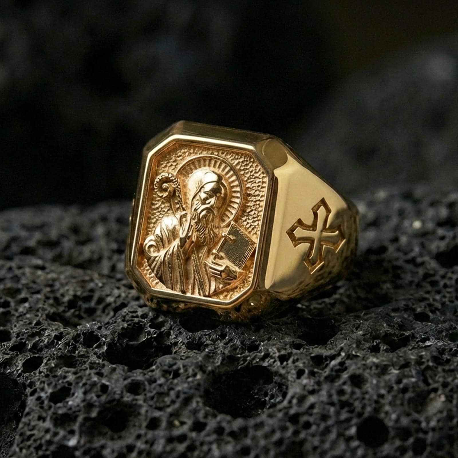 Gold plated Saint Benedict signet ring on dark volcanic rock, detailed saint engraving, cross side accent