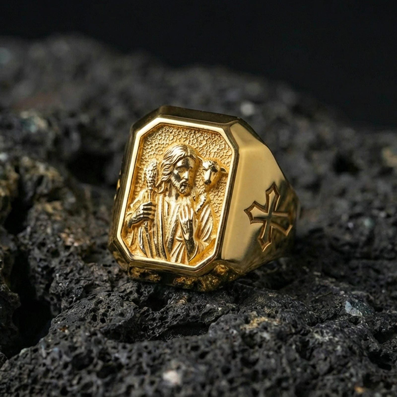 Gold plated Jesus Shepherd signet ring on dark volcanic rock, lamb motif relief, cross shoulder detail close-up