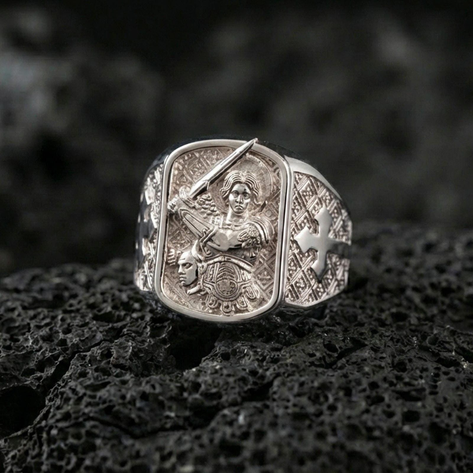 Polished silver Saint Michael signet ring on porous volcanic stone, archangel with sword engraving, cross side detail close-up