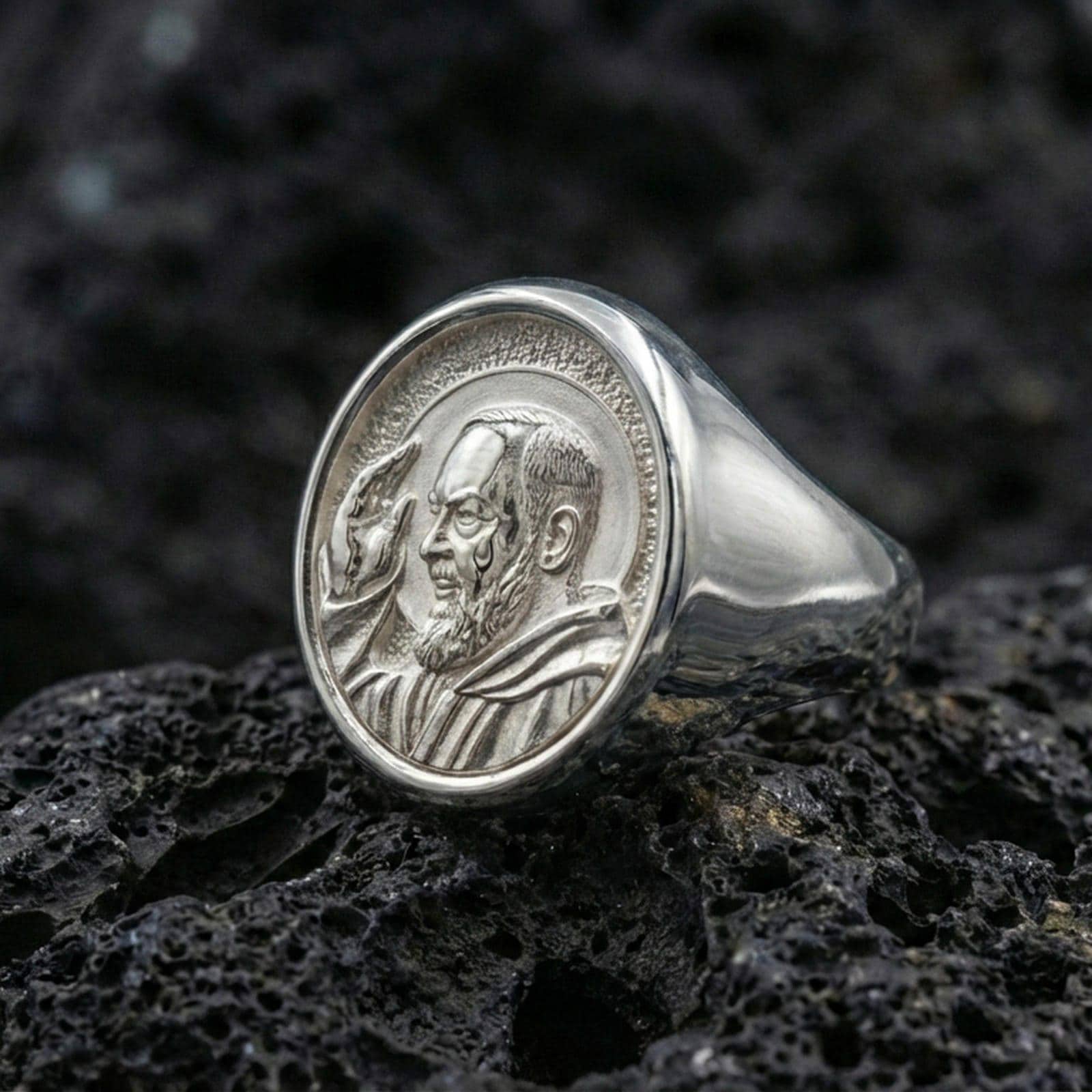 Polished silver Padre Pio ring on porous volcanic stone, detailed saint profile engraving, religious signet ring