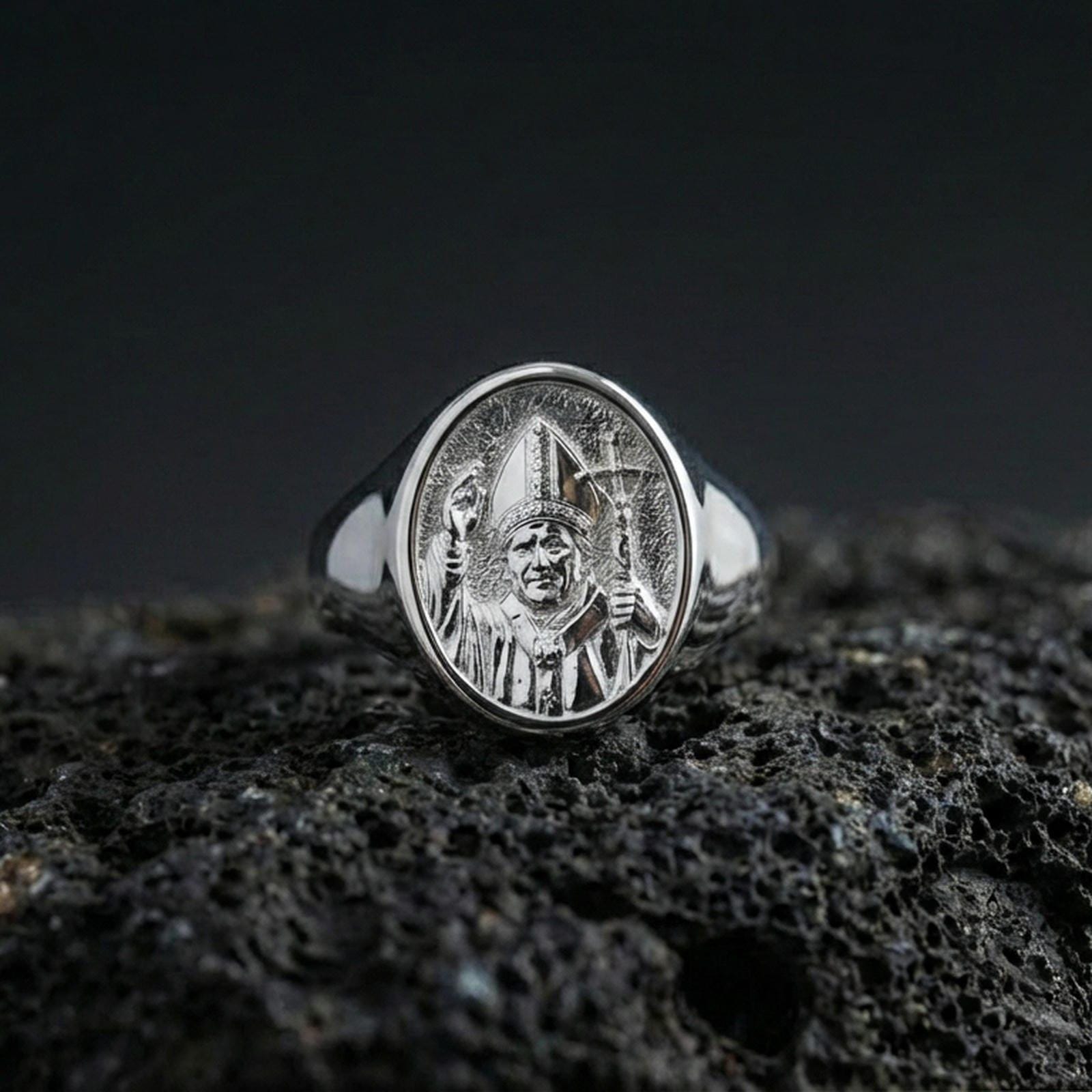 Polished silver Pope John Paul II ring on porous volcanic stone, detailed papal portrait engraving, Catholic signet ring